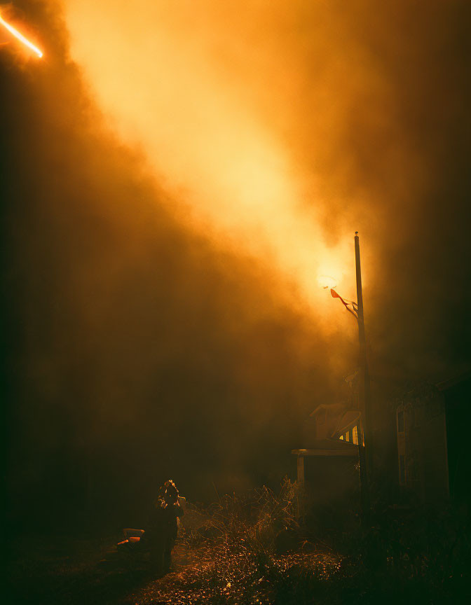 Silhouetted Figure Near House Under Amber Sky with Streetlight and Light Streak