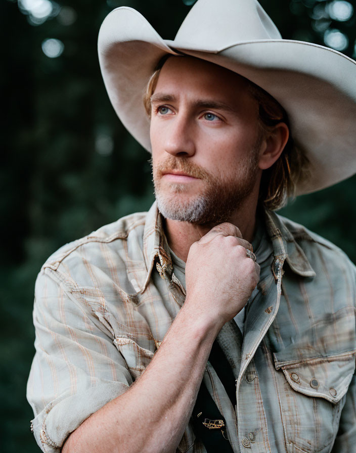 Bearded man in cowboy hat and plaid shirt, contemplating outdoors