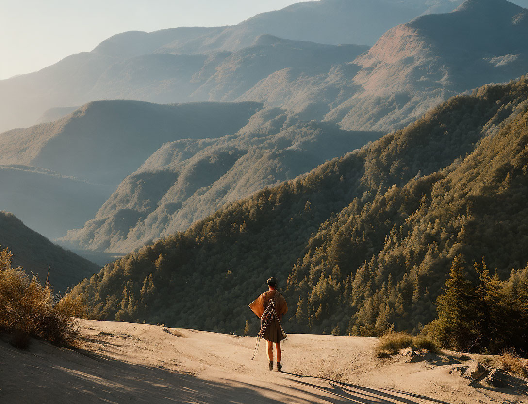 Hiker with backpack on dusty trail, sunlit mountains, green valleys