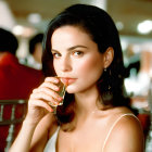 Dark-haired woman in white holding glass, smiling at camera, blurred background.