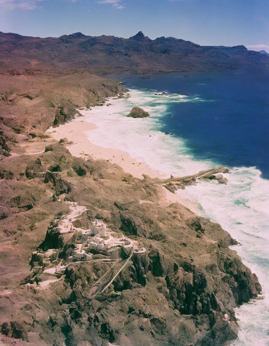 Rocky Coastal Landscape with Sandy Beach and Buildings under Blue Sky