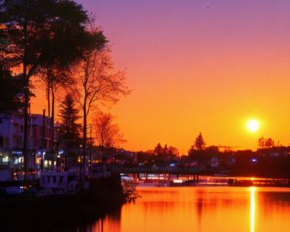 Vibrant sunset reflected in calm river with silhouetted trees and distant city lights