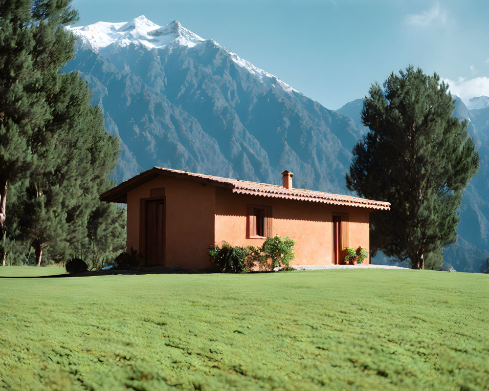 Tranquil landscape with brown house, green lawn, mountains, blue sky