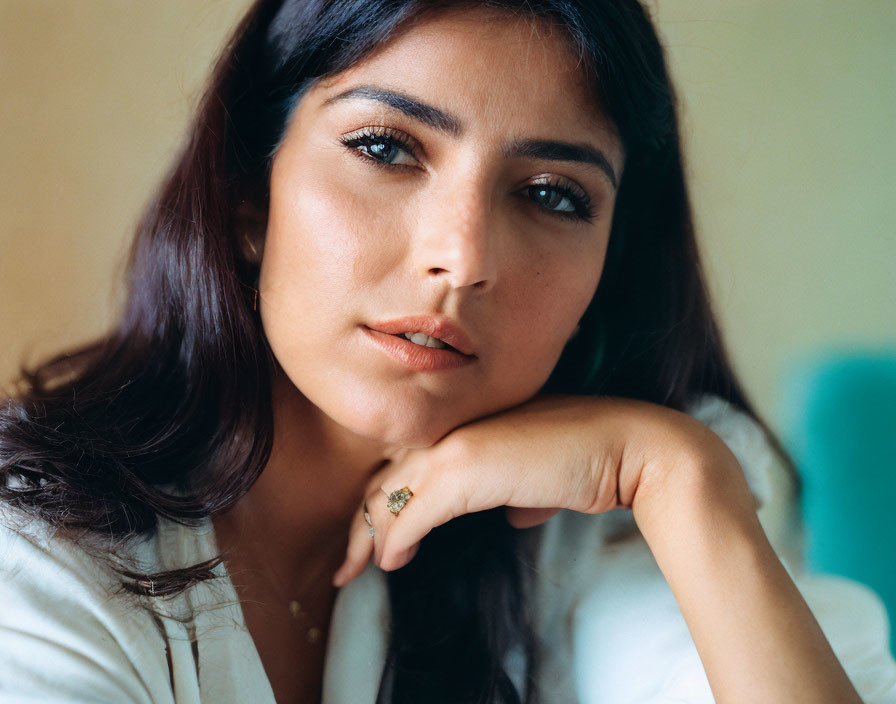 Dark-haired woman in light blouse gazes thoughtfully at camera