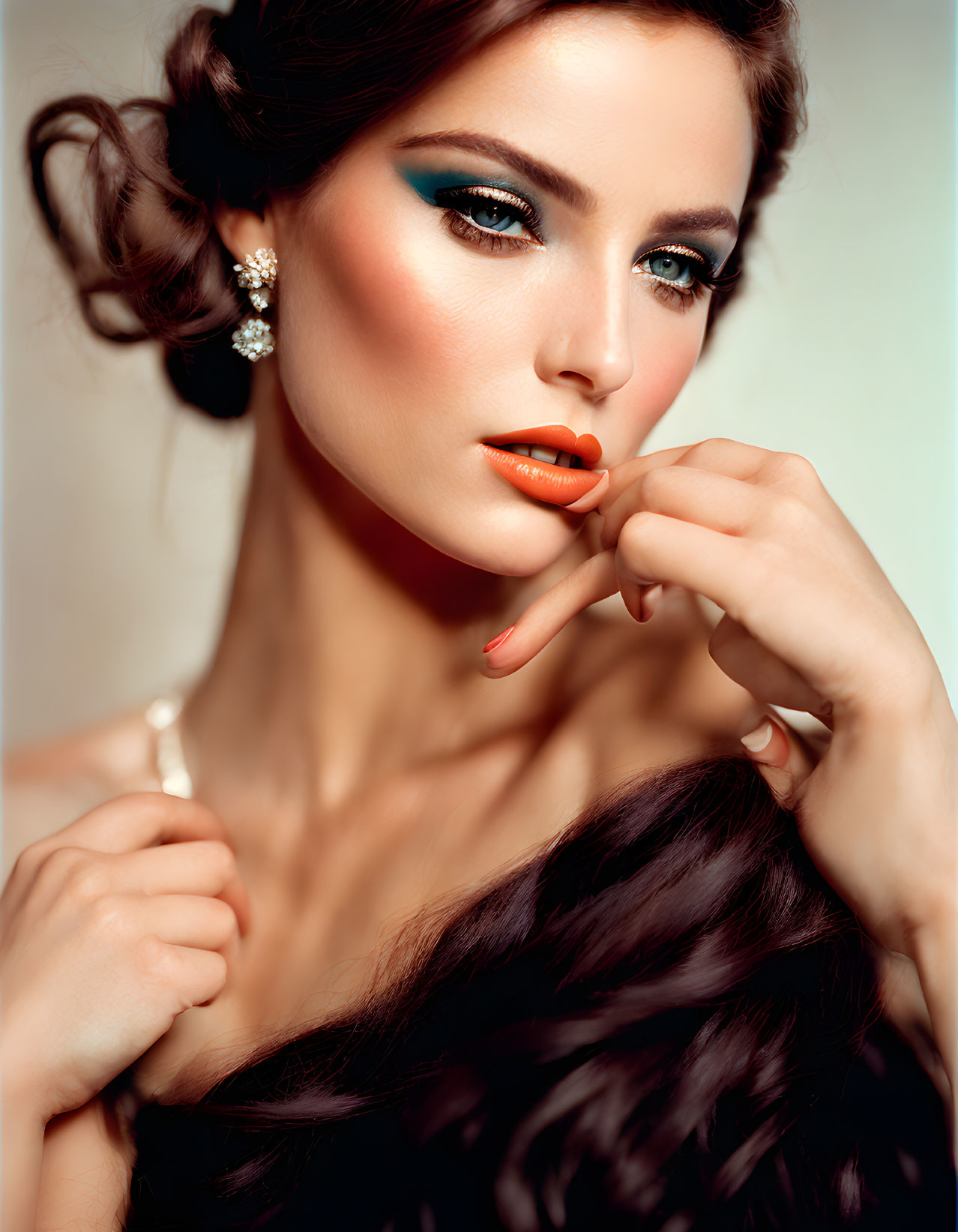 Woman with dramatic makeup displaying vibrant orange nail polish and elegant hairstyle