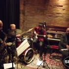 Live jazz band performance with saxophonist, drummer, pianist, and bassist in dimly