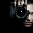 Surreal portrait of woman with camera lens eye & butterflies on dark background