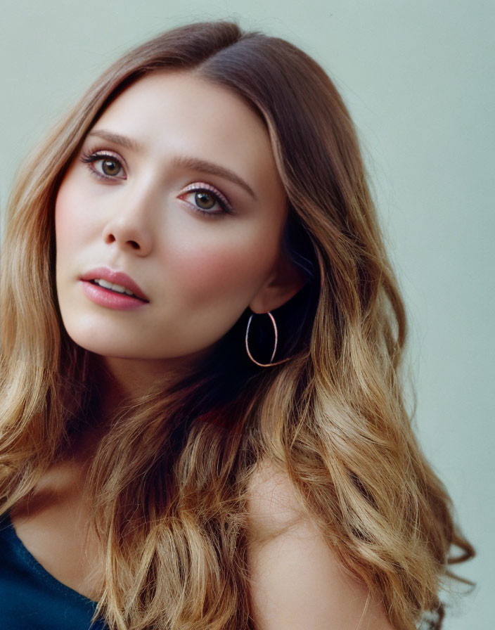 Portrait of woman with wavy hair and hoop earrings on light background