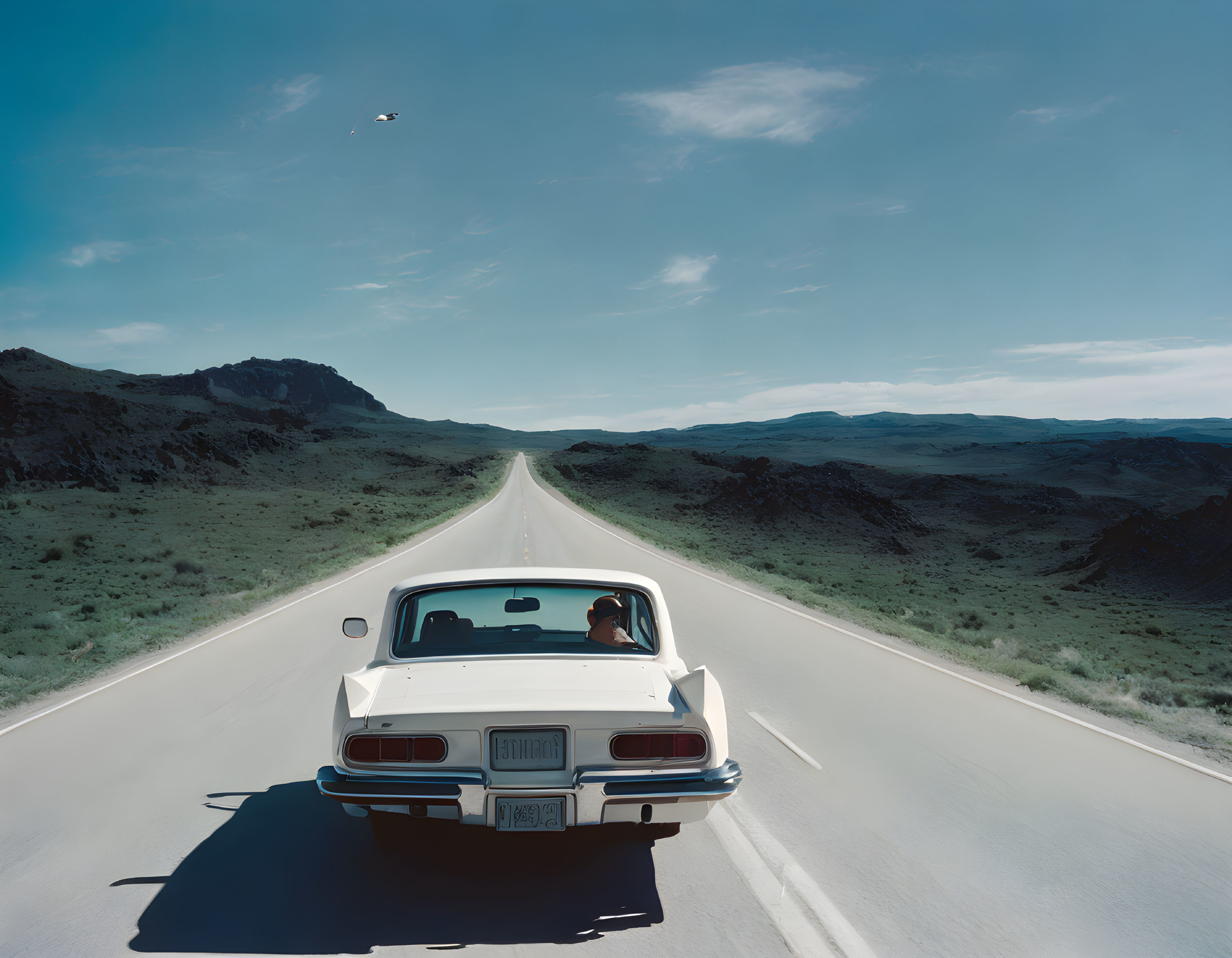 Vintage White Car Driving on Open Road in Desolate Landscape with Clear Sky