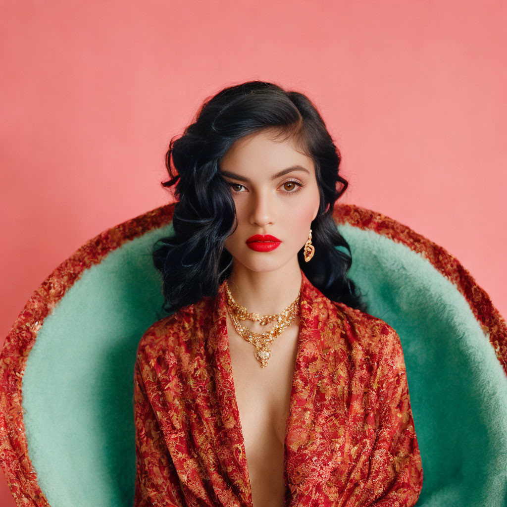 Dark-haired woman in red lipstick, gold jewelry, and red robe on pink background