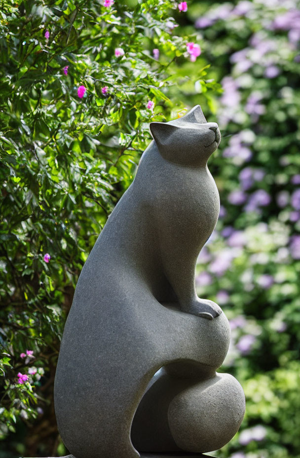 Stone Cat Sculpture Among Greenery and Pink Flowers