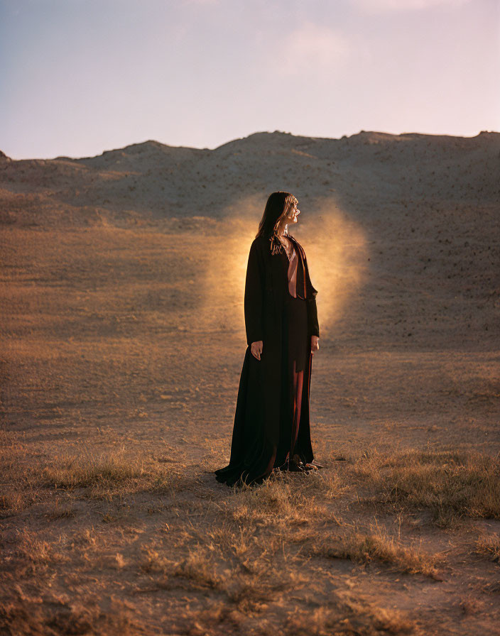 Silhouetted figure in dark robe standing in desert under sun halo.