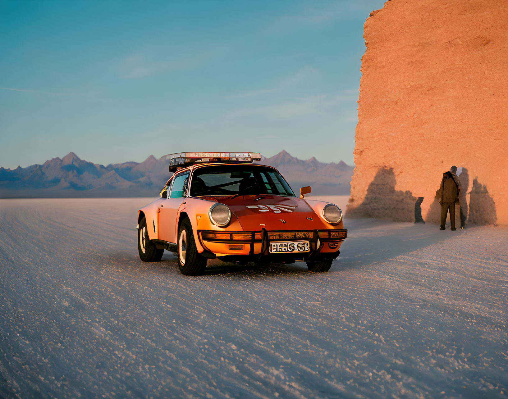 Orange Vintage Sports Car on Salt Flat Terrain at Sunset with Mountains and Person Walking Towards Salt Formation