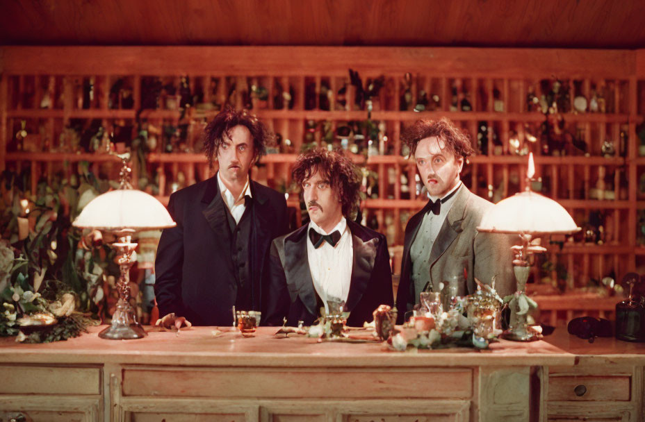 Three men in vintage suits with messy hair behind a bar, holding drinks and looking puzzled.