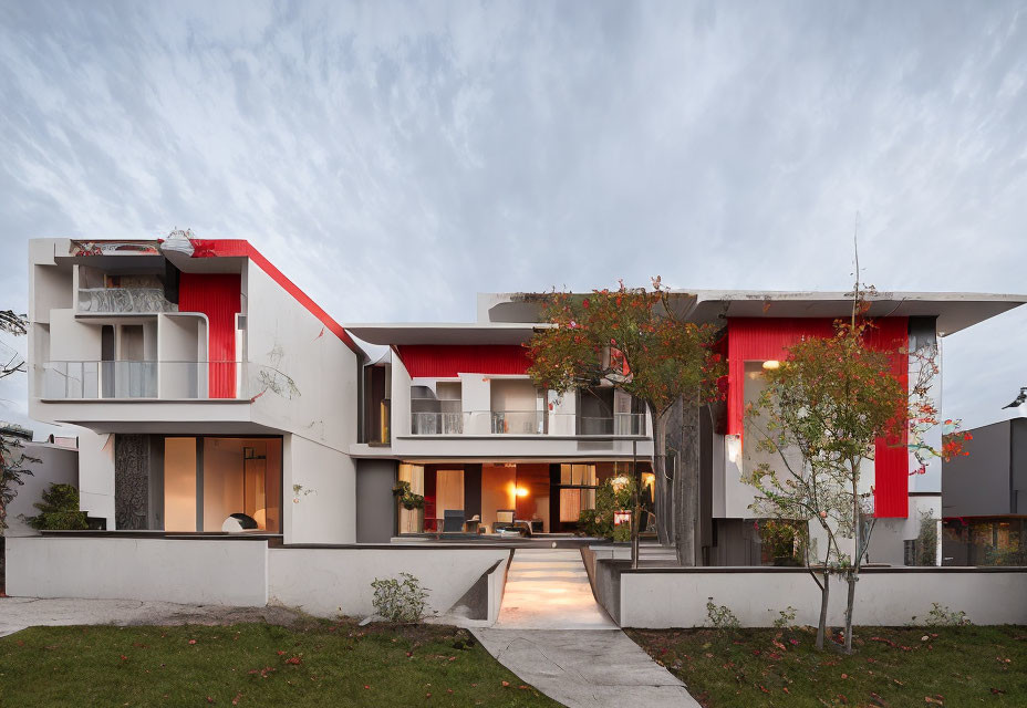 Contemporary two-story house with white walls, red accents, flat roofs, balconies, and illuminated