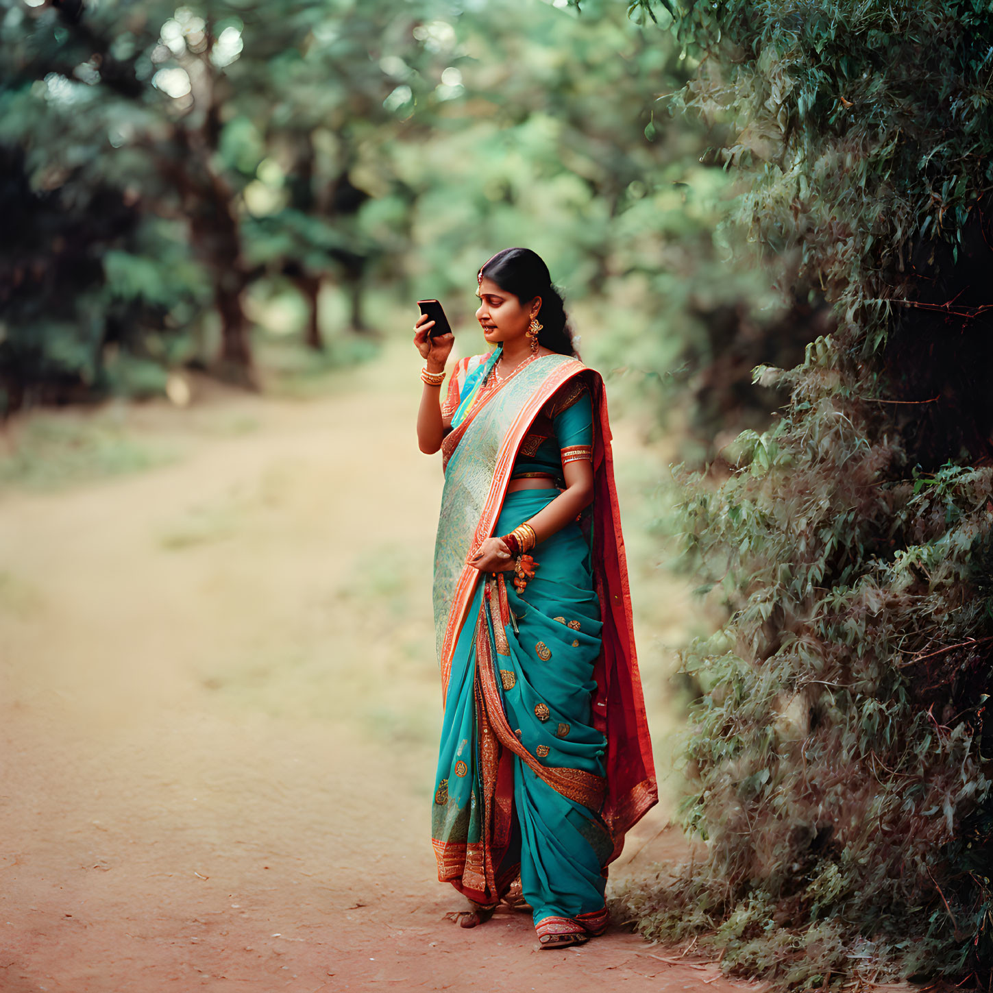 Woman in green and orange sari on dirt path with smartphone