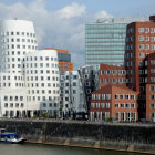 Golden skyscrapers and white buildings in futuristic cityscape with boats on water under cloudy sky