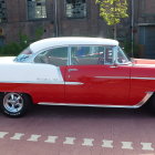 Vintage car with white top and wood paneling parked by red brick houses, showing two people inside.