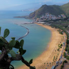 Tranquil seaside landscape with beach, clear waters, hills, cacti, and village