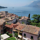 Tranquil lakeside villa with terracotta roofs nestled amidst greenery and distant mountains under a