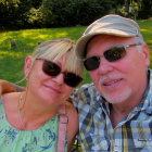 Happy couple in sunglasses on park bench with flowers and trees