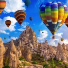 Colorful hot air balloons over autumn landscape with lake, rocks, and trees