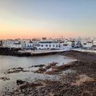 Tranquil coastal sunset with white houses, calm ocean, black rocks, sandy beaches, clouds,