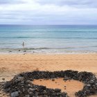 Golden sand beach with rocky outcrops, crashing waves, distant island, and cloudy sky