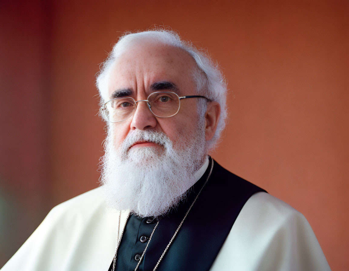 Elderly man with white beard and round glasses in black clerical attire on orange background