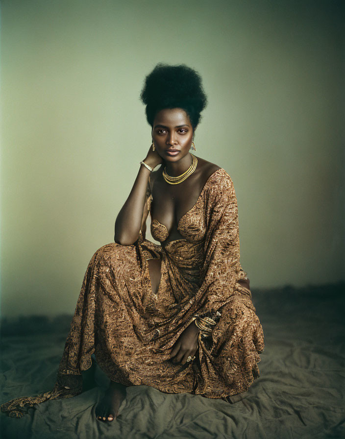 Poised individual with afro hairstyle in golden-brown textured dress against muted background