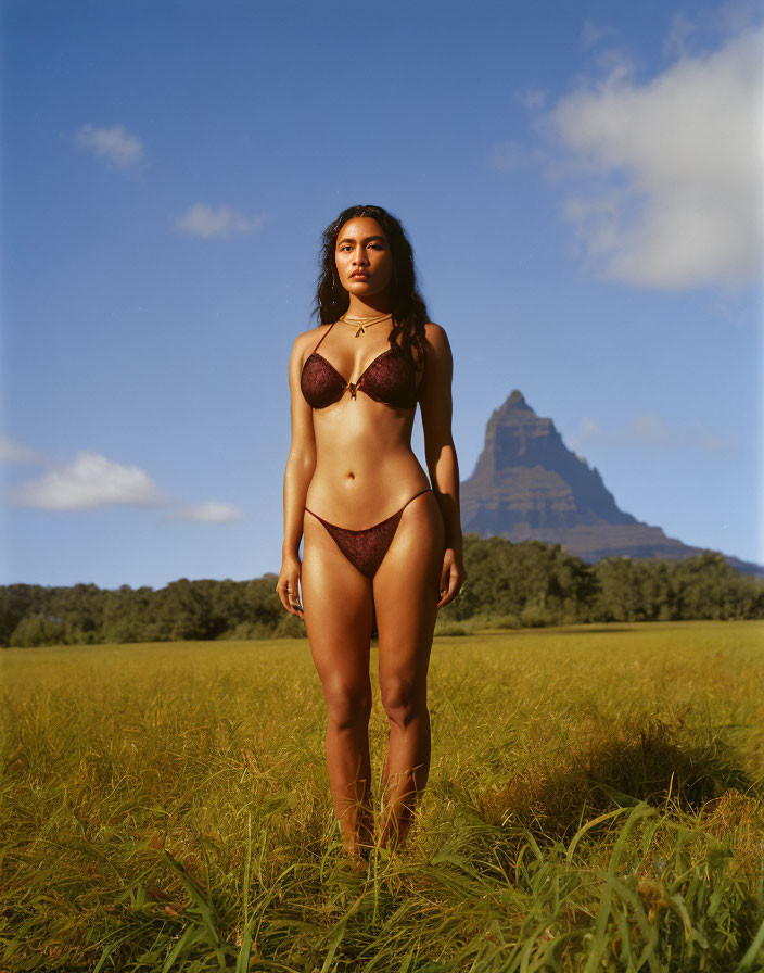 Woman in Burgundy Bikini in Field with Mountain and Blue Sky