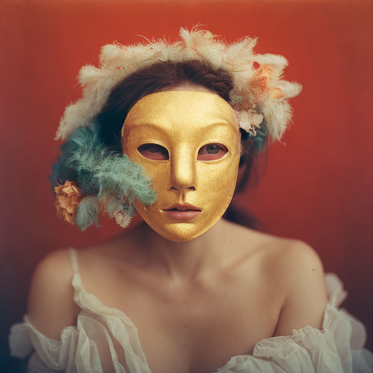 Person posing with gold mask, feathers, and flowers on red backdrop