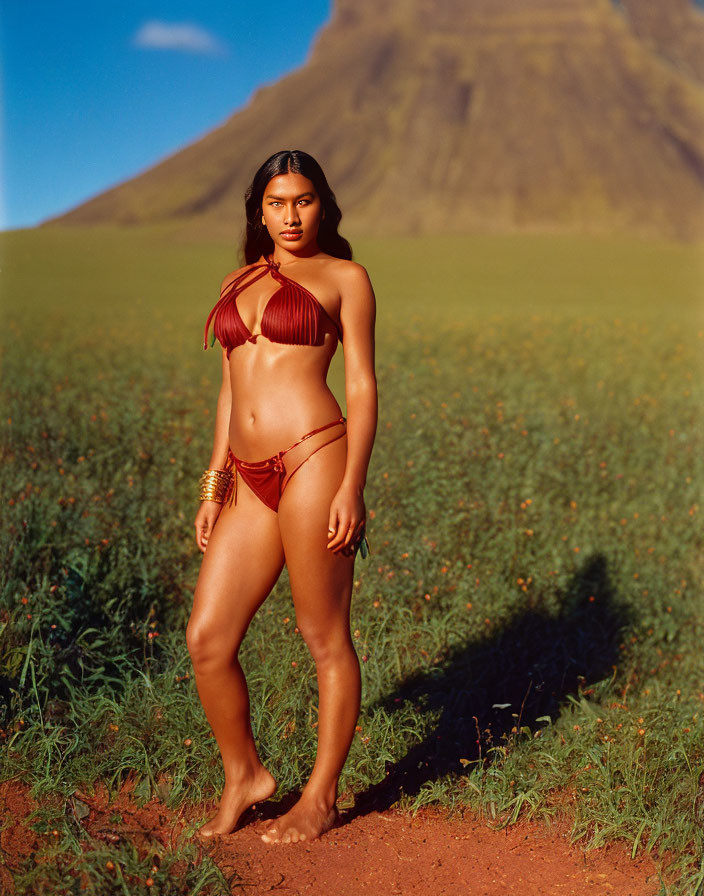 Red Bikini and Gold Accessories in Green Field with Hill and Blue Sky