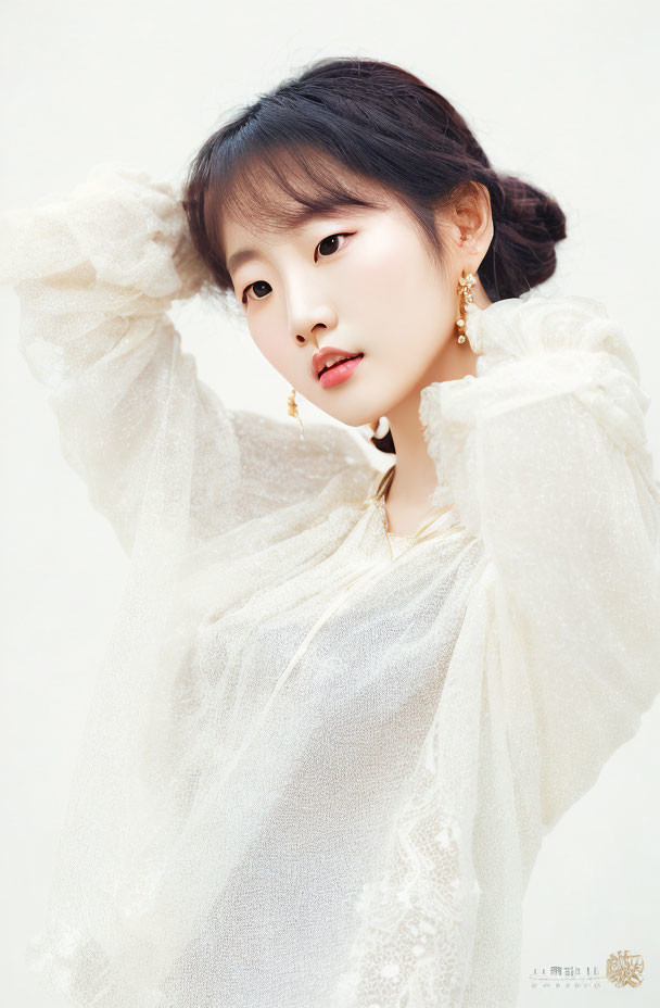 Dark-haired woman in white sheer blouse with voluminous sleeves and gold earrings posing with hands by head