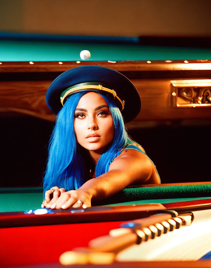 Blue-haired person in peaked cap leaning on pool table gazes at camera