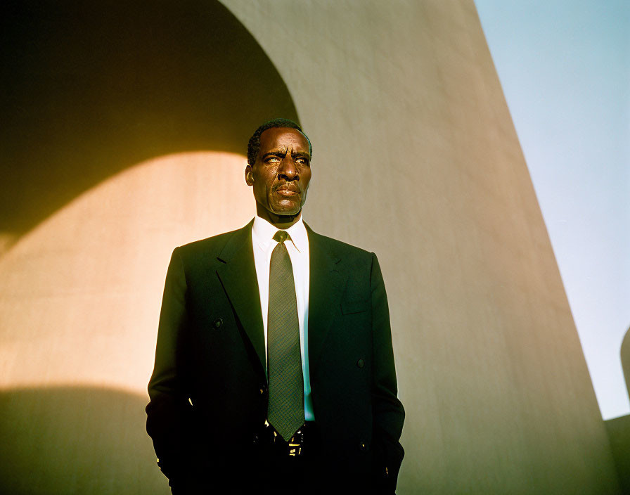 Confident man in dark suit against geometric backdrop with sunlight