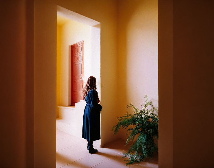 Person in Blue Robe Contemplating by Open Doorway in Yellow Room