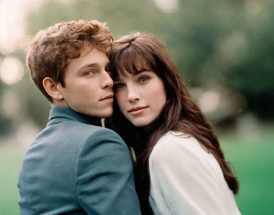 Young couple embracing tenderly in park, man looking at camera, woman resting head.