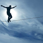 Tightrope walker balances above clouds with sunbeam silhouette