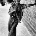 Historical woman with rifle and broom leaning on stone wall