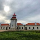 Vibrant red-roofed lighthouse against dramatic sky and calm sea