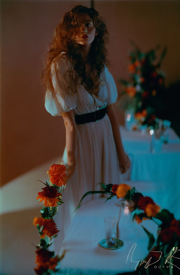 Vintage Cream Dress Woman Standing Behind Table with Flowers in Moody Room