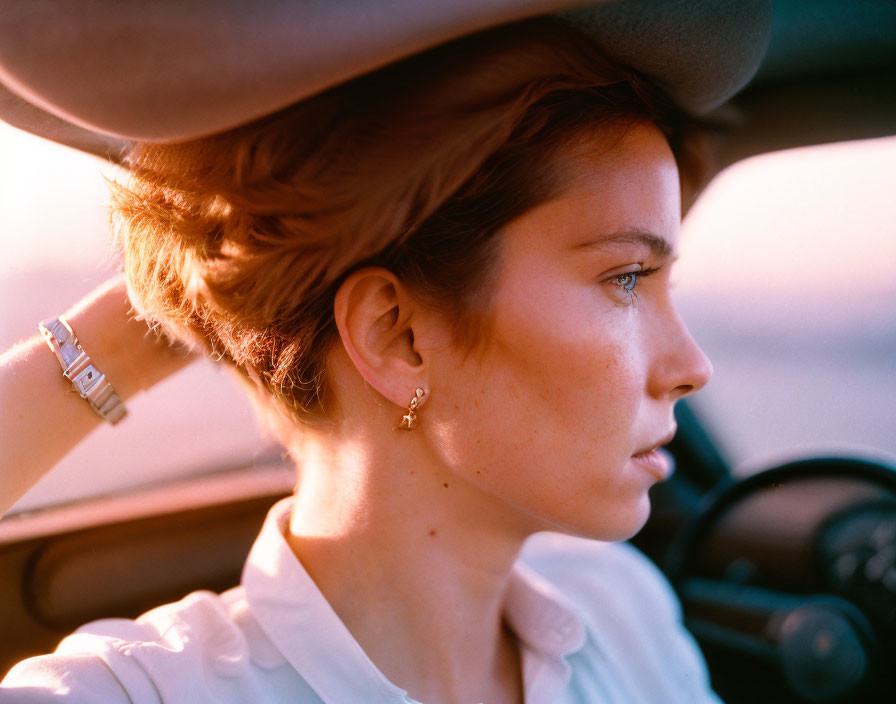 Woman in sun hat sitting in car, profile illuminated by golden hour sunlight.