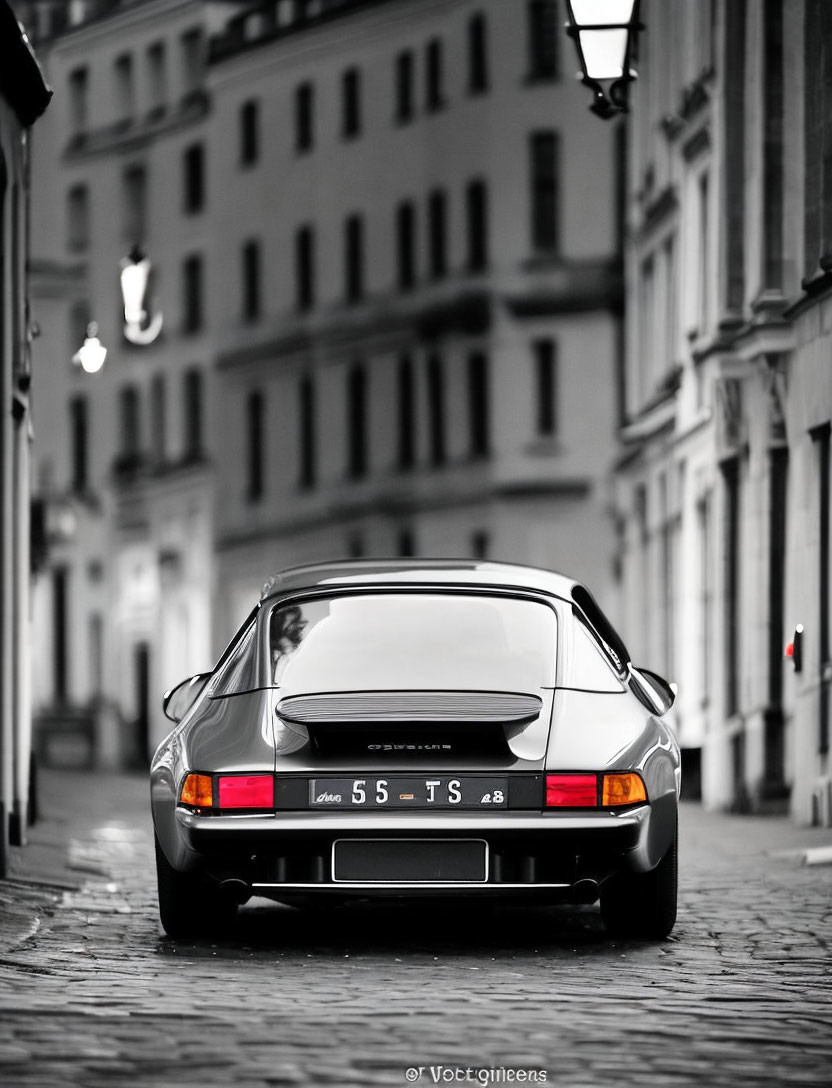 Vintage Porsche 911 parked in cobblestone alley in black and white, with colored tail lights