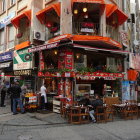 Colorful street scene with cafe, pedestrians, bicycles, and cars under blue sky