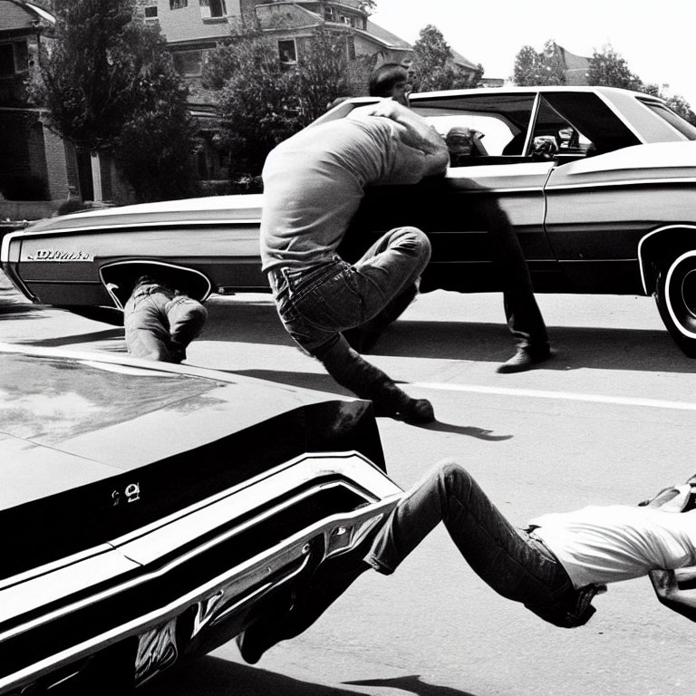 Monochrome image of men leaping over vintage cars, suggesting motion.