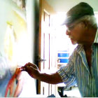 Elderly man in cap with lobster at table near open window with green foliage