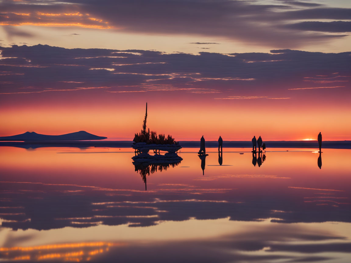 Vivid orange sunset reflected on water with silhouettes of people.