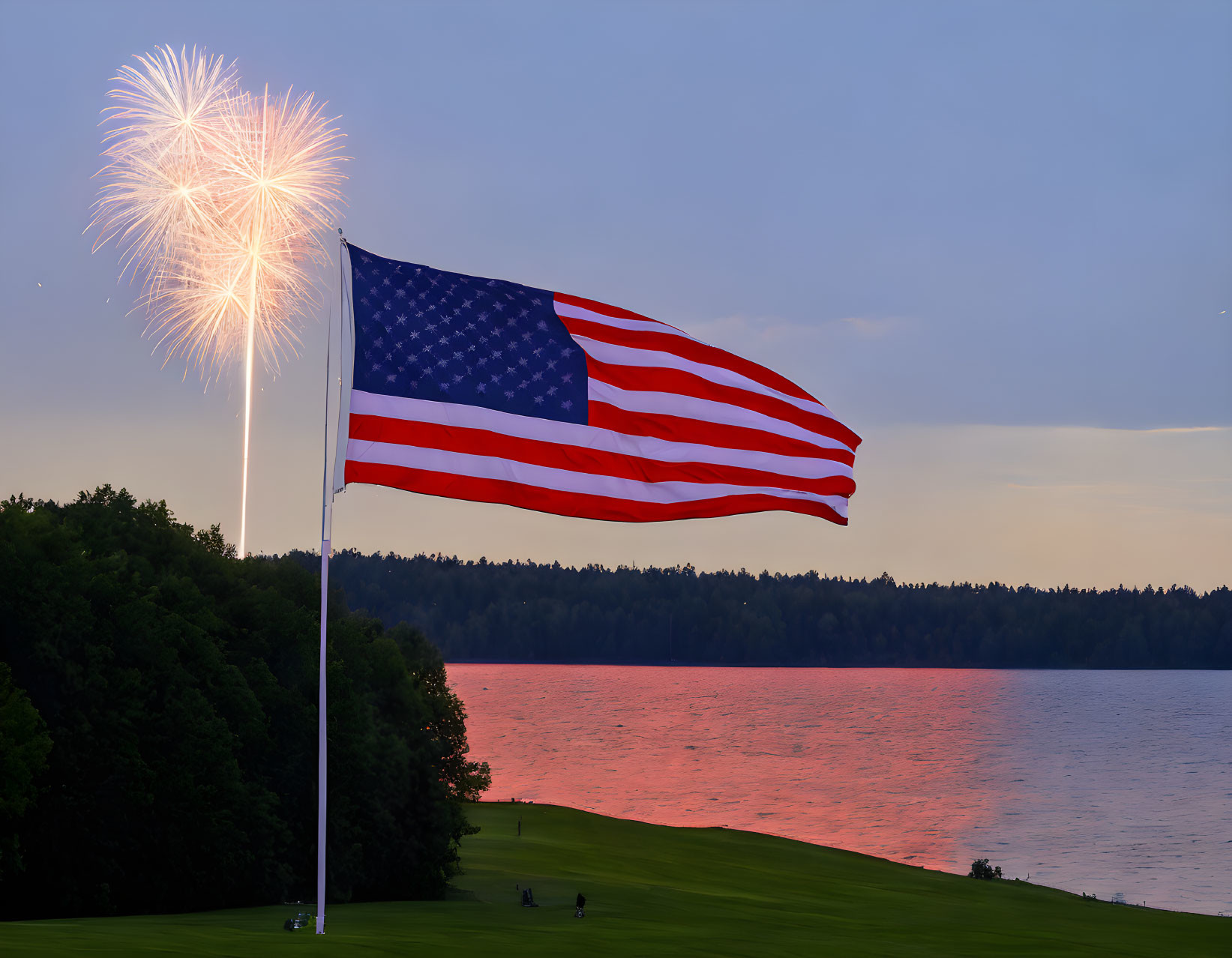 American flag waving at sunset over calm lake with fireworks display