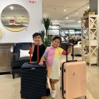 Three children in stylish outfits with luggage in an airport terminal.